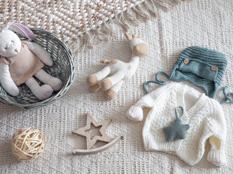 Brassière en tricot et jouets en bois pour bébé posés sur une table, illustrant la préparation de la liste de naissance à Caen.