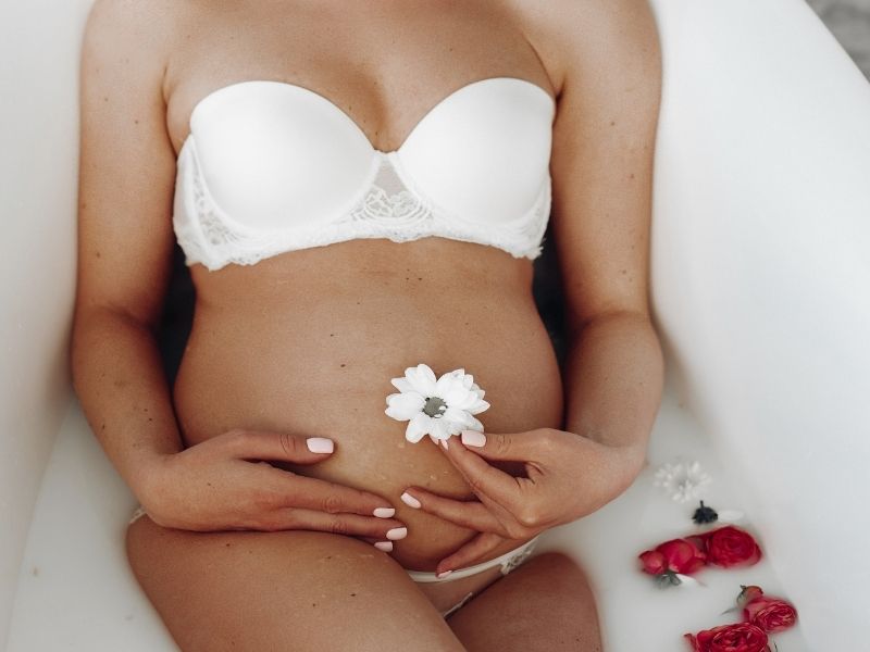 Femme enceinte se relaxant dans un bain et tenant une fleur, illustrant l’importance de l’organisation et de la sérénité de la maman.