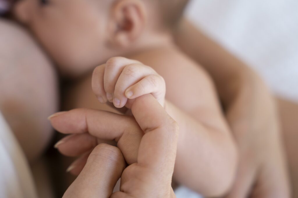 Gros plan sur un nouveau-né tenant le doigt de sa mère pendant l'allaitement, illustrant les services de baby planning à Caen pour le post-partum.