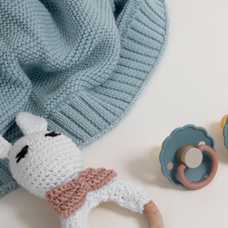Tétine, doudou et couverture de naissance pour nouveau-né posés à plat, symbolisant la puériculture durable en Normandie.