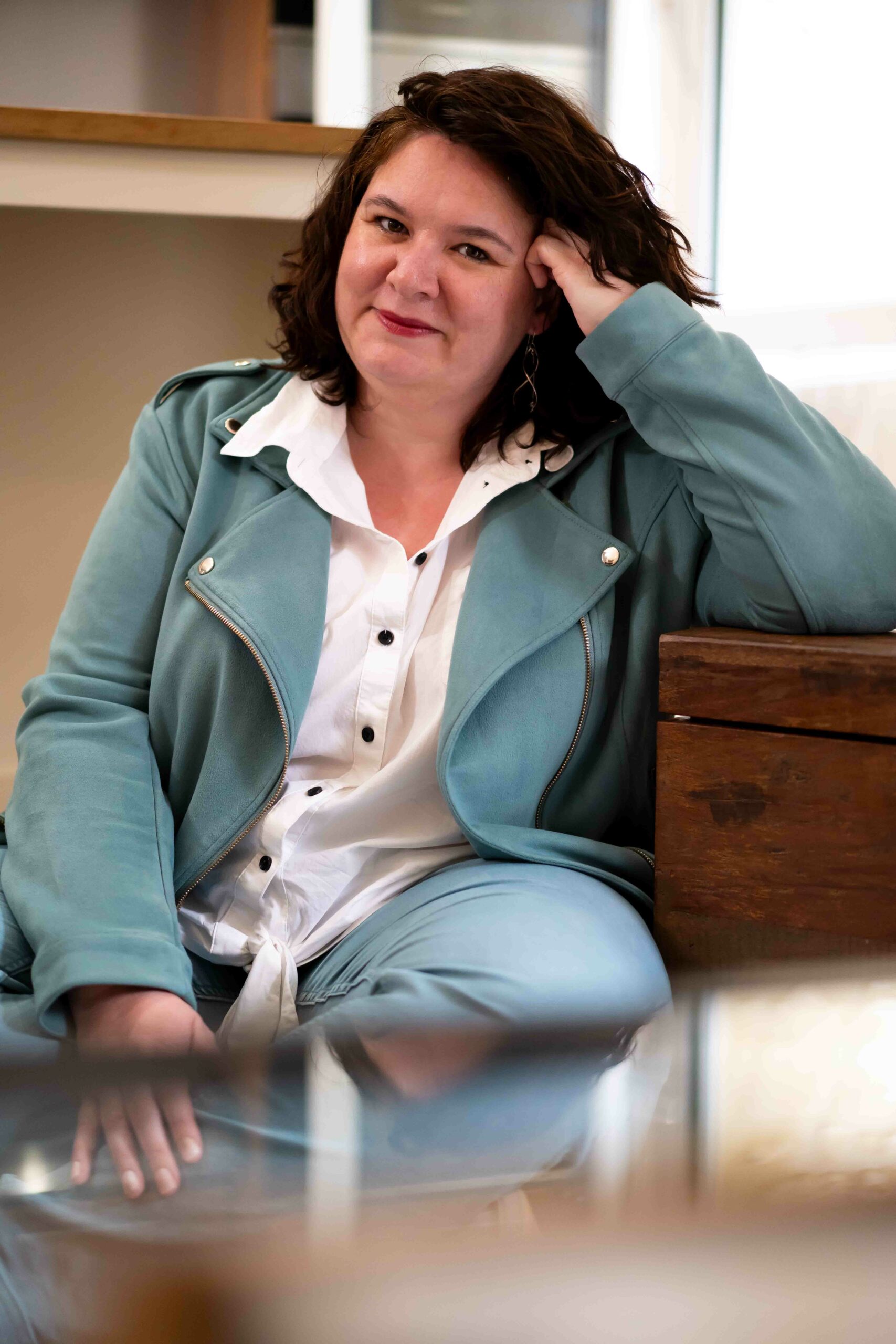 Portrait de Maureen assise par terre en tailleur et souriante face à l'objectif, incarnant l'accompagnement des futurs parents en Normandie.